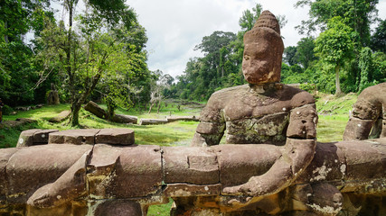 A statue with ruined face holding the fence of the road outside the ancient city of the Khmer empire - Angkor Thom. (Angkor Wat, Siem Reap, Cambodia)