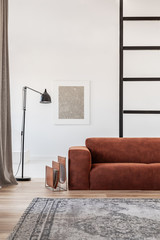Black industrial lamp next to fashionable scandinavian sofa in bright living room interior