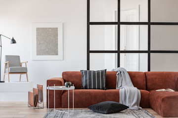 Silver abstract painting in white frame on the wall of trendy living room interior with brown corner sofa © Photographee.eu