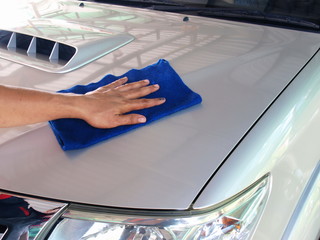 Men's hands are cleaning the car with a microfiber cloth.