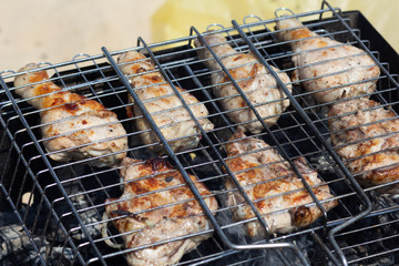 Grilled parts of chicken on the grill cooking on smoldering coal outdoors