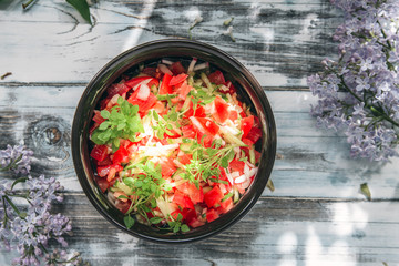clay cup with vegetable salad from tomato, cucumbers and a basil on fonederevyanny the old table decorated by branches of the blossoming lilac