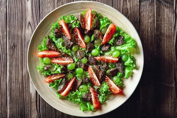 warm salad with chicken liver and grapes on a wooden table