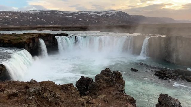 The extremely popular waterfall Godafoss filmed from the tourist plateau on a magical evening with dramatic colours in the sky and the snowcovered mountains surrounding the waterfall