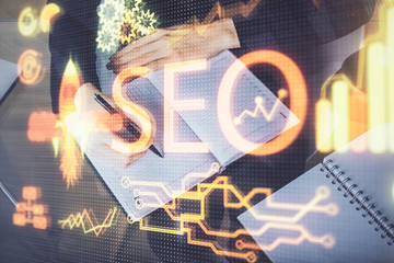 Multi exposure of woman's hands making notes with SEO icon. Concept of Search engine optimization