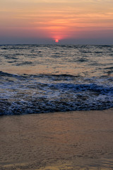 Beautiful colorful sunset on the ocean, vertical photo. Sand beach, the sun sets in the clouds above the sea.