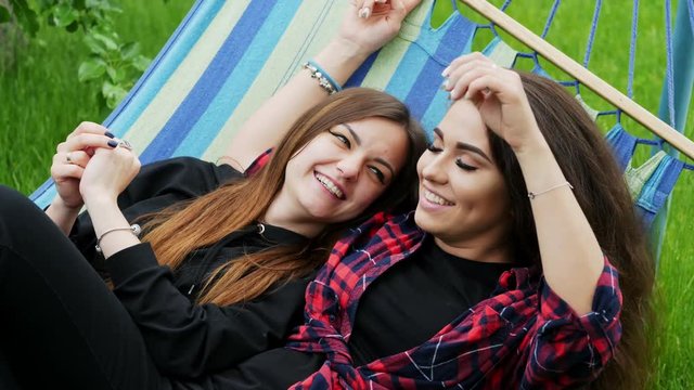 Lesbian girlfriends lie in hammock in garden. Two lesbians woman hug and laugh, lgbt concept