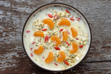 Fresh breakfast of granola, yogurt, nuts, goji berries, chia seeds and mandarin. Muesli with fruits and berries in bowl on a wooden background