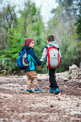 Two boys with backpacks are walking along a forest path.