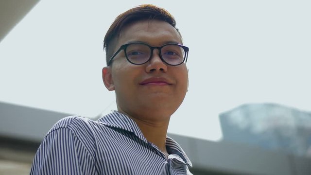 Slow motion portrait asian businessman smiling and looking at camera standing on urban city. Low angle shooting.