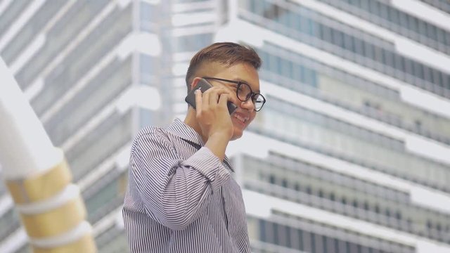 Slow motion portrait asian businessman answers the phone. Asian man with glasses use phone in street near big office building.