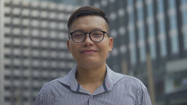 Portrait handsome asian businessman smiling and looking at camera standing on urban city. Slow motion shoot.
