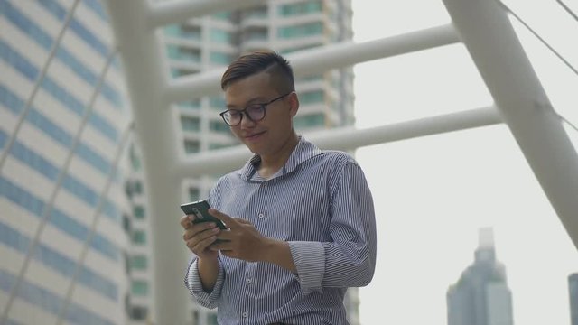 Portrait handsome asian businessman smiling and using mobile phone send message with friend standing on urban city. Slow motion shoot.