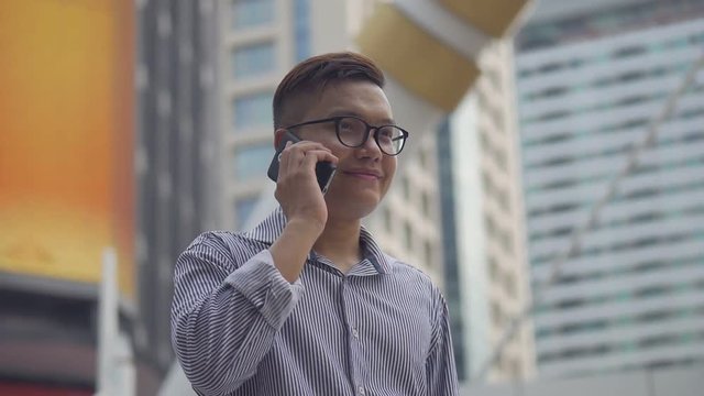 Slow motion portrait asian businessman answers the phone. Asian man with glasses use phone in street near big office building.