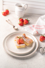 a dessert, vanilla cake with sugar powder and strawberry, on a plate, on a light marble backdrop, 