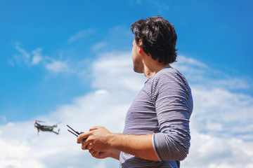 Young Man watching and navigating a flying drone in blue clear Sky