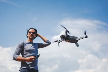 Young Man watching and navigating a flying drone in blue clear Sky