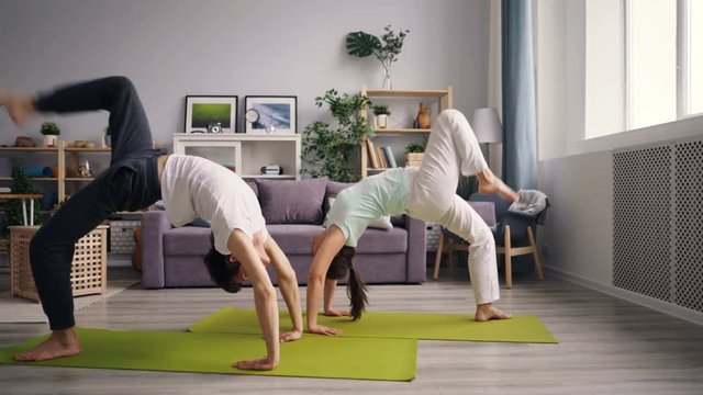 Young family doing gymnastics at home exercising in crab position on floor standing on hands and feet then raising legs. Youth, people and sports concept.
