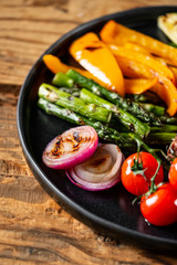 Grilled and sliced vegetables served on black plate on old rustic wood background.