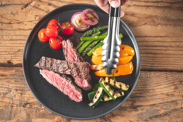 Chef hands serving meat steak and vegetables assorted cooked on grill.