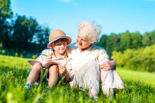 Attractive grandmother with her grandson are learning school assignments outdoors together. A boy with a granny is studying for the summer holidays. Self-education and development