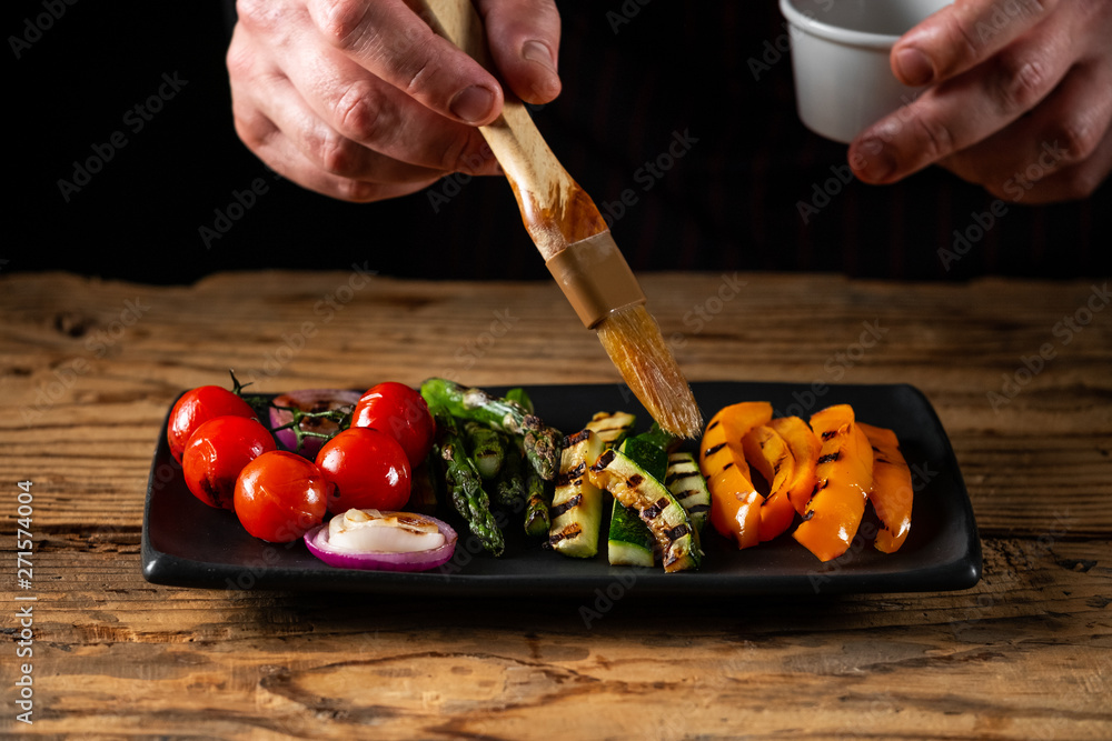 Wall mural chef cooking grill vegetables assorted on black plate on wooden table background.