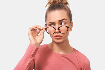 Studio closeup portrait of young woman frowning puzzled faces. Beautiful female woman looking through transparent eyewear at someone aside. People and emotions concept