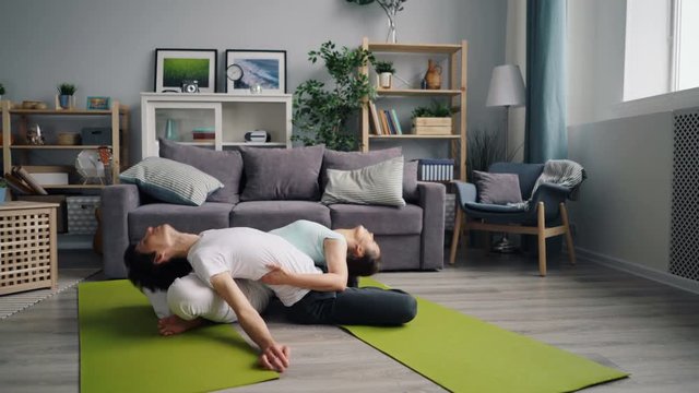 Attractive guy and girl flexible young people are doing pair yoga exercises in flat sitting on floor on mats. Healthy active lifestyle and relationship concept.