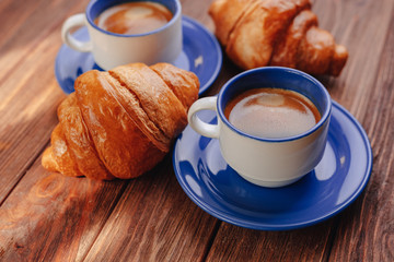two cups of coffee and croissants on a wooden background, good light, morning atmosphere