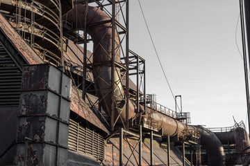 Exterior of industrial steel manufacturing complex showing pipes and rusting steel structures, horizontal aspect
