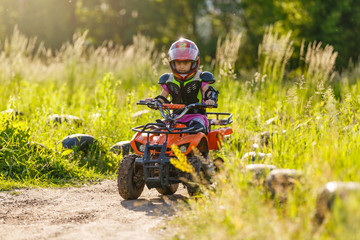 The little girl rides a quad bike. A mini quad bike is a cool girl in a helmet and protective...