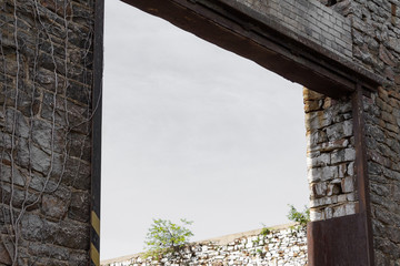 Rusted metal framework in open archway of wall with stones and brick, open sky behind, horizontal aspect