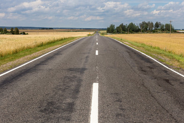 Fototapeta premium Widok małej drogi asfaltowej na wsi z błękitne niebo i chmury cumulus w tle.