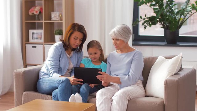 family, technology and three generations concept - happy mother, daughter and grandmother with tablet computer at home