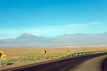 Desert road curve in Atacama: yellow sign and barren landscape of desert