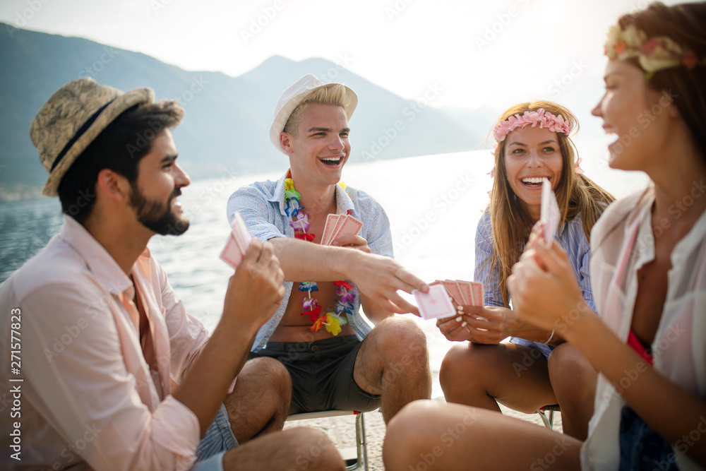 Poster group of young friends having fun while playing cards on beach