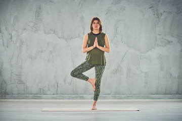 Fototapeta premium Charming brunette standing on the mat in half lotus pose.