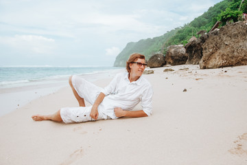 Fototapeta na wymiar red-haired man in white clothes resting on a white beach