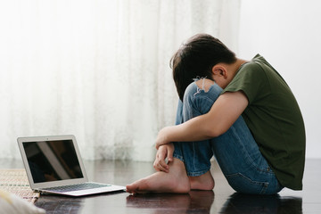 Cyberbullying and Depression. Asian teenage boy sitting alone and hugging knees, putting face down...