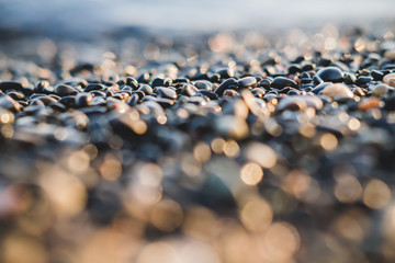Obraz premium Small stones by the sea with bokeh effect. Blurred decorative background, place for text. Summer wallpaper, sunny sunset light.