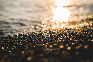 Small stones by the sea with bokeh effect. Blurred decorative background, place for text. Summer wallpaper, sunny sunset light.