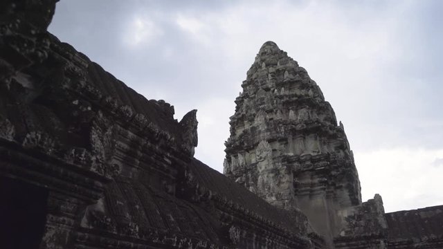 Looking up and walking towards the central shrine at Angkor Wat against a partly cloudy sky.