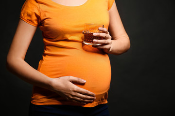 Pregnant woman with glass of alcohol on dark background
