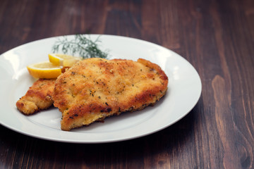 fried chicken with lemon on white plate on brown wooden background