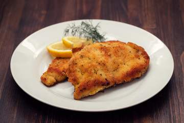 fried chicken with lemon on white plate on brown wooden background