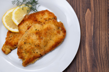 fried chicken with lemon on white plate on brown wooden background