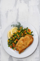 fried chicken with boiled vegetables and lemon on white dish