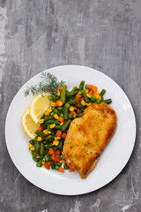 fried chicken with boiled vegetables and lemon on white dish