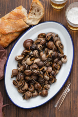 boiled snails with herbs in white dish on wooden  background