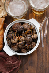 boiled snails with herbs in white bowl and glasses of beer on brown wooden  background